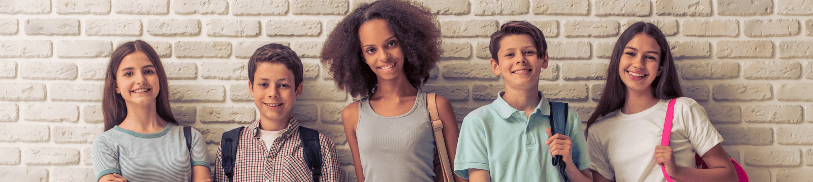 Kids smiling with backpacks against a wall