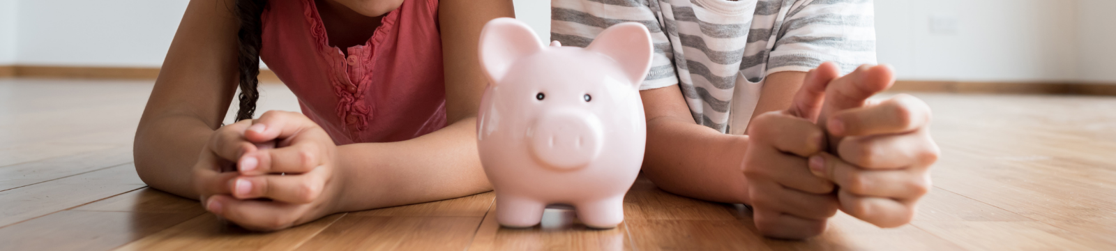 Two kids laying on a floor with a piggy bank between them